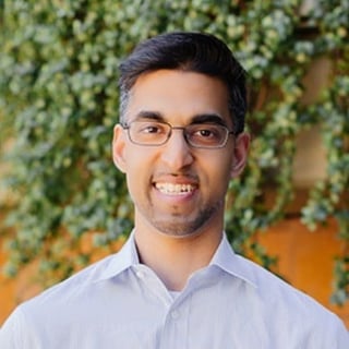 Man with glasses and light blue shirt smiling at camera against ivy wall background